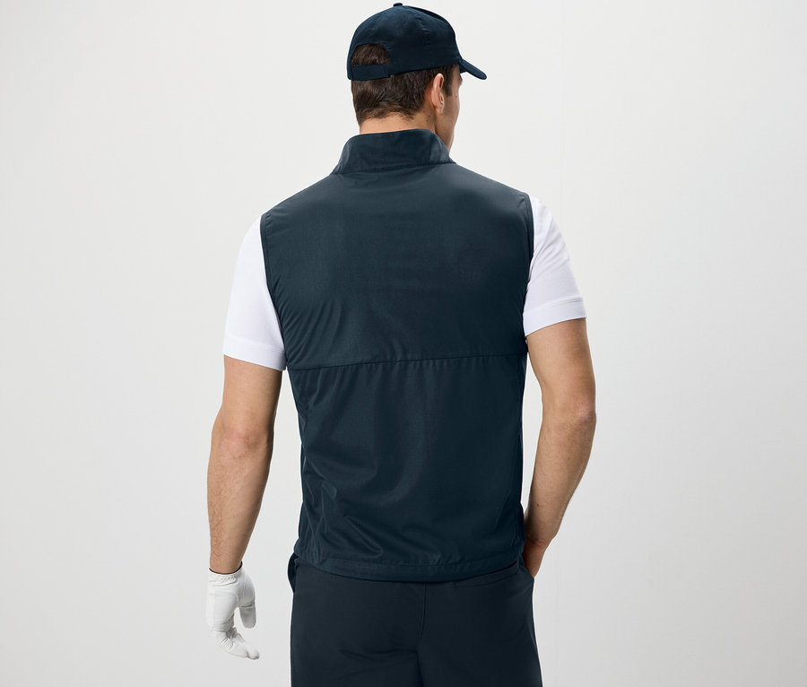 Háttal álló férfi softshell mellényt, pólót és baseball sapkát visel.