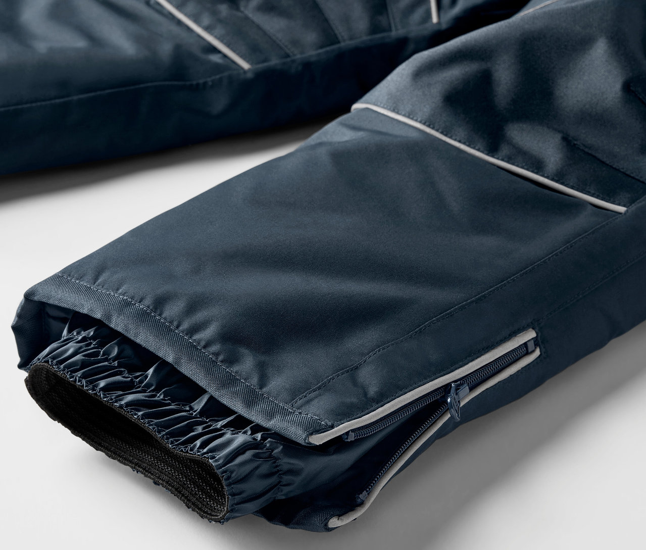 Egy sötétkék síelőnadrág szárának részletfotója, elasztikus mandzsettákkal és cipzárral.