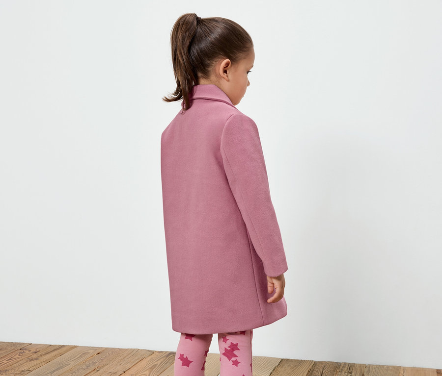 Egy kislány rózsaszín kabátban és csillagmintás leggingsben áll háttal a kamerának.