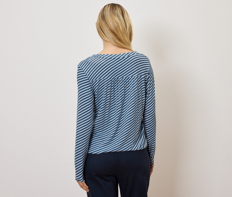 Hátulnézet egy szőke hajú nőről, aki kék-fehér csíkos felsőt és sötétkék nadrágot visel.