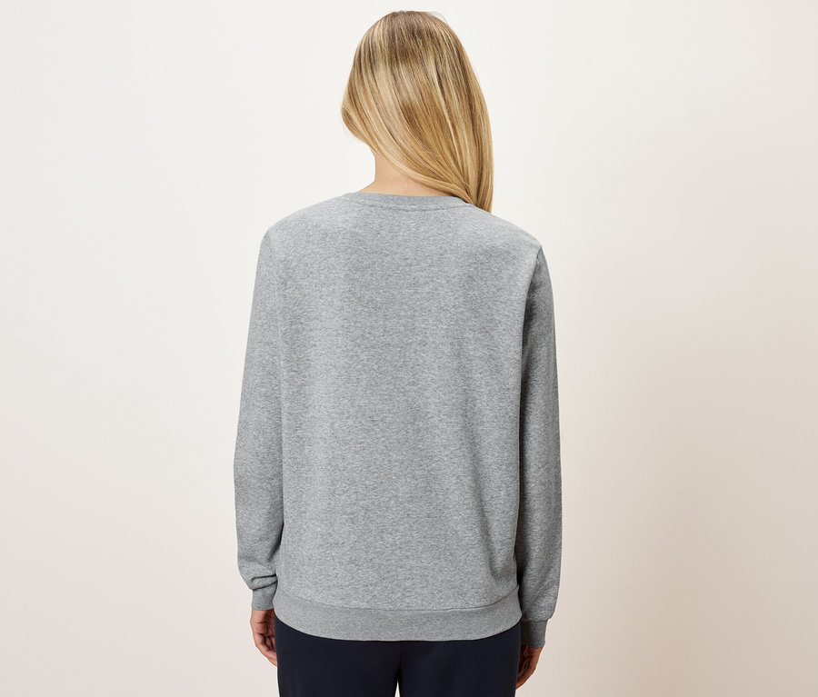 Hátulnézet egy szőke hajú nőről, aki szürke pulóvert és sötétkék nadrágot visel.