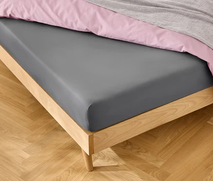 Ágy szürke lepedővel, rózsaszín ágyneművel és szürke takaróval.