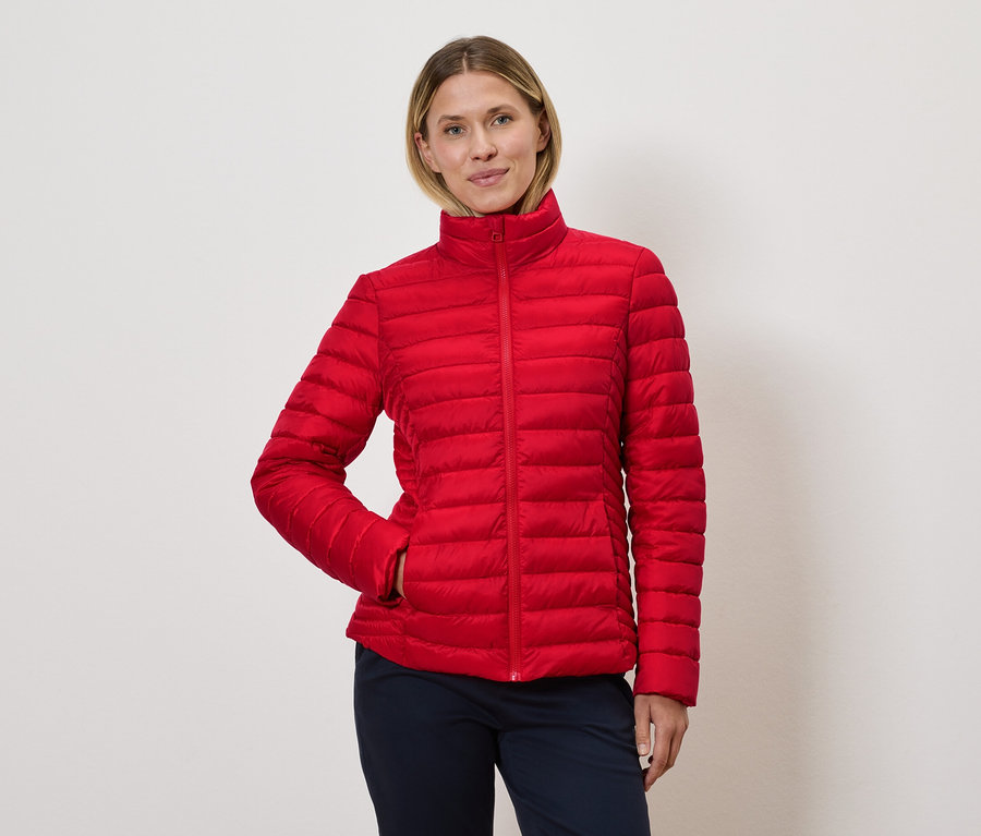 Nő pózol piros steppelt kabátban.