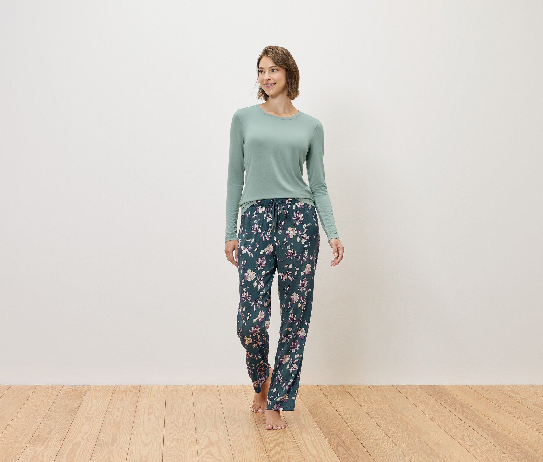 Egy nő mezítláb sétál, mentaszínű pulóvert és sötétkék, virágmintás pizsamanadrágot visel.