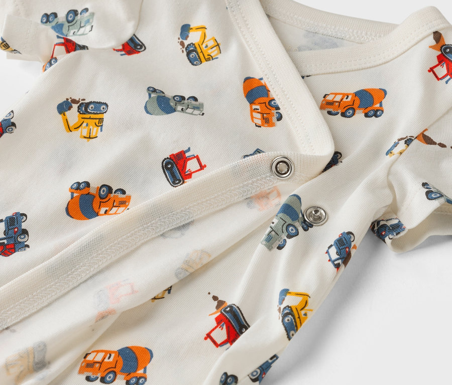 Közeli kép egy fehér, építőipari autó mintás babaruháról.