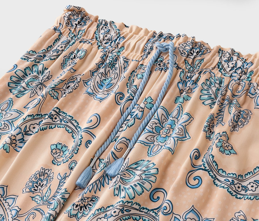 Közeli kép egy barack színű, kék virágmintás és húzózsinóros nadrágról.