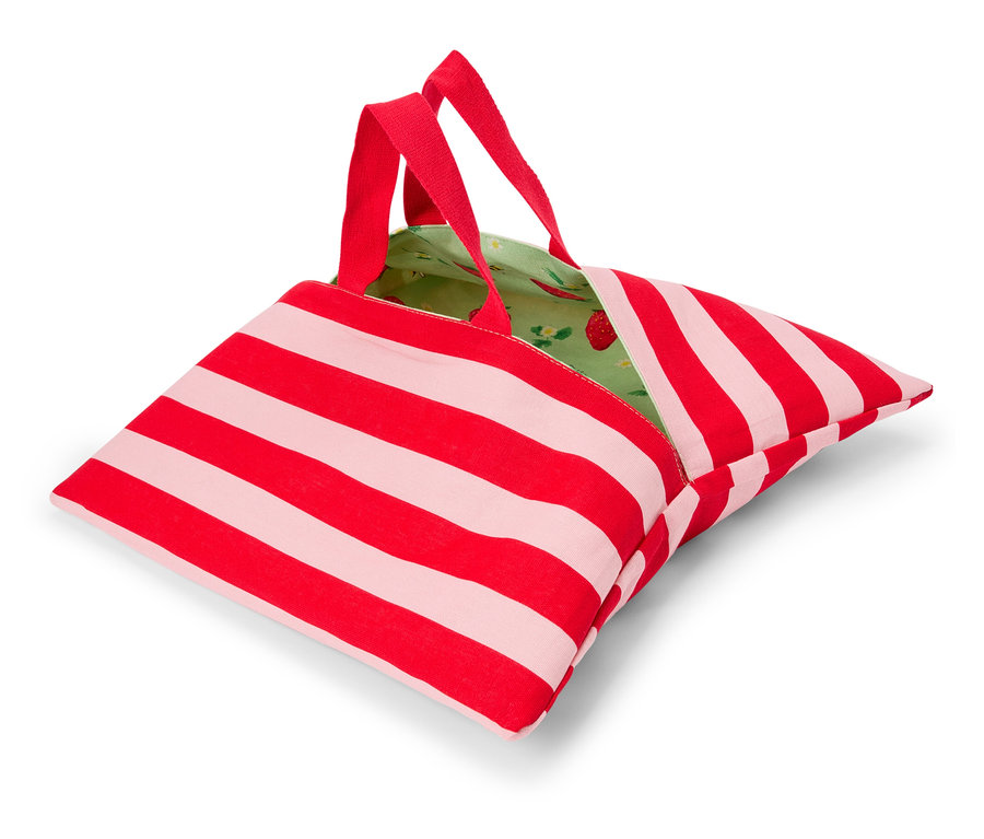 Egy piros-fehér csíkos táska piros fogantyúkkal és zöld, eper mintás béléssel fekszik egy fehér felületen.