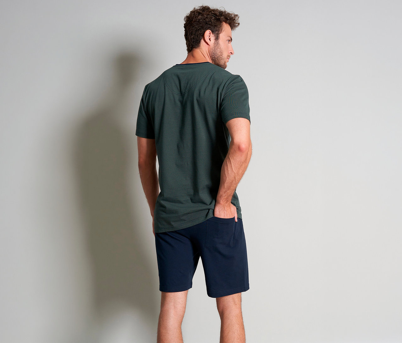 Hátulról látható férfi zöld Tom Tailor »Nevada« rövidnadrágos pizsamában, egyik kezével a zsebében.