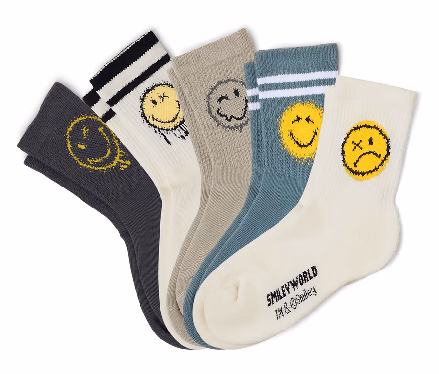 Öt pár SMILEYWORLD® gyerek tenisz zokni fehér, szürke és petrolkék színekben, legyezőszerűen elrendezve. Minden zoknin más, kopottas sárga vagy szürke smiley arc látható, némelyik csíkos mandzsettával.