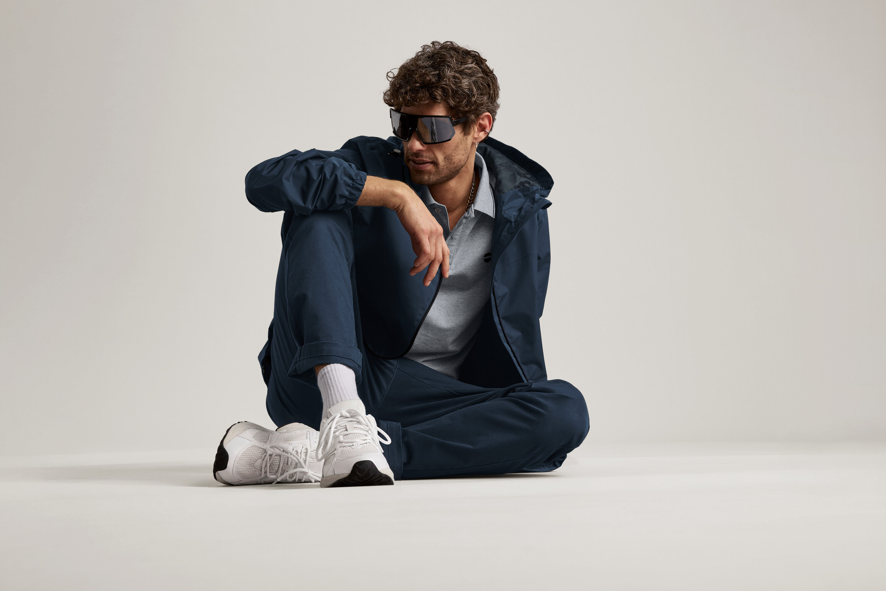 Egy férfi ül a padlón, tengerészkék chino nadrágot, kabátot és napszemüveget visel.