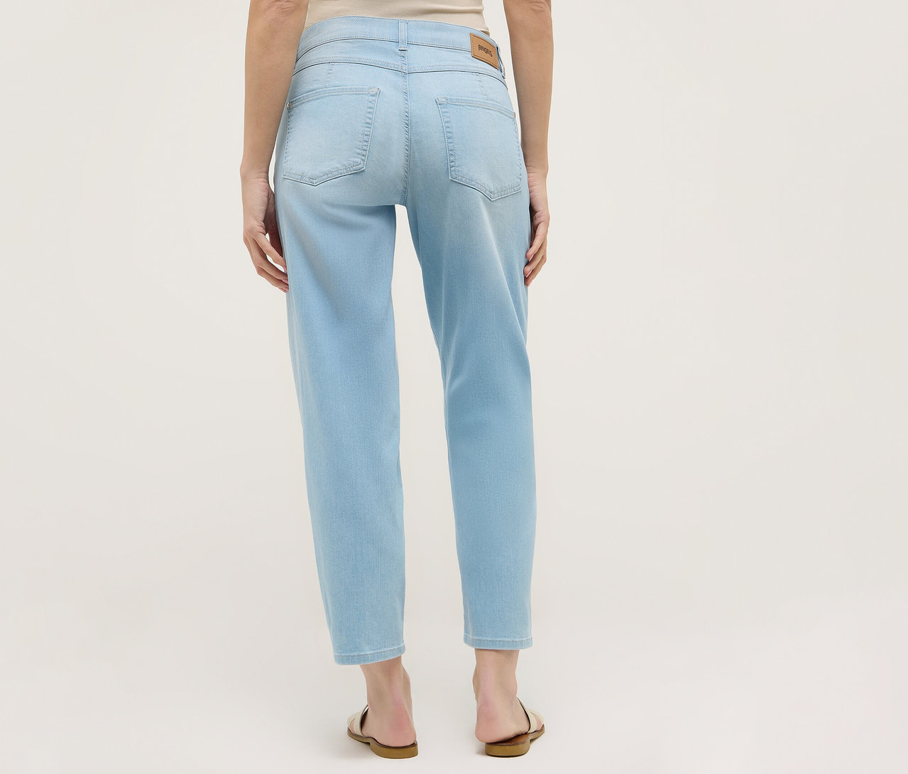 Hátulnézet egy világoskék Angels Denim »Evy Cool« O alakú farmernadrágot és szandált viselő nőről.