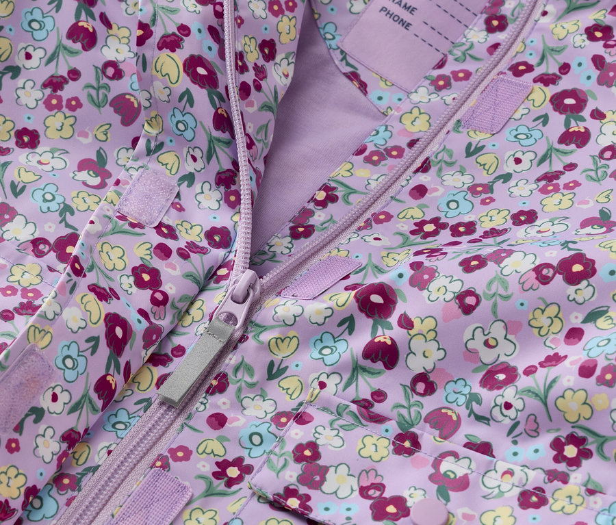 Egy lila, virágmintás gyerekdzseki közeli képe, cipzárral nyitva.