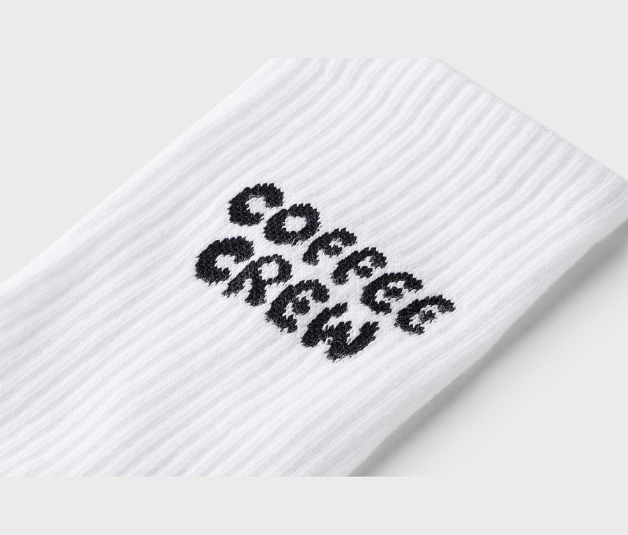 Közeli kép egy fehér zokniról, fekete "Coffee Crew" felirattal.