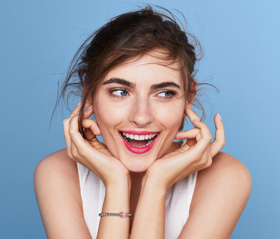 Mosolygó nő világoskék háttér előtt, karkötőt visel.