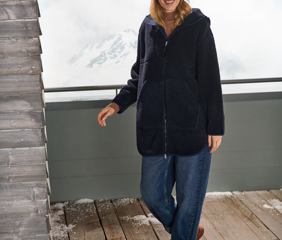 Nő sötétkék női oversize plüsskabátot, farmert és sapkát visel.