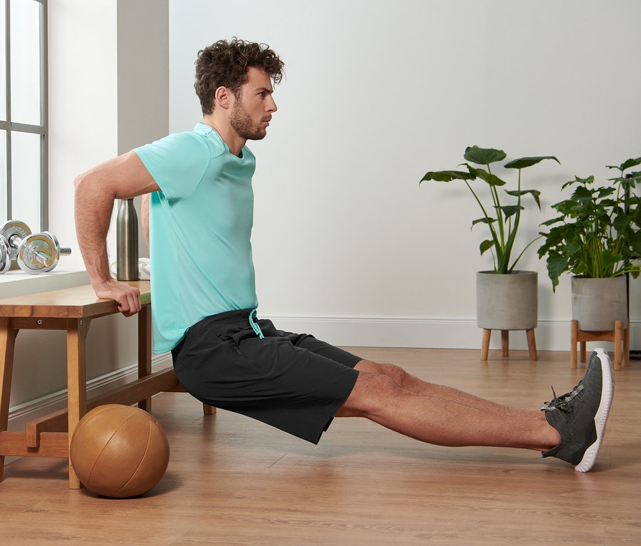 Férfi tricepsz-dipszet végez egy padon, és fekete férfi sport rövidnadrágot visel.