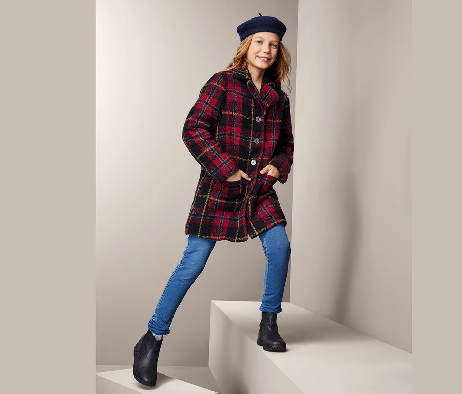 Lány kockás kabátban, kék farmerban és fekete csizmában pózol.