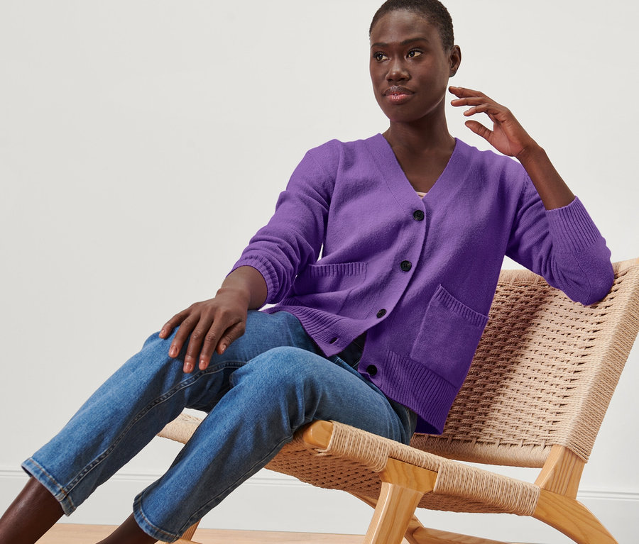Nő ül egy székben, és lila, gyapjú kötött kardigánt visel.