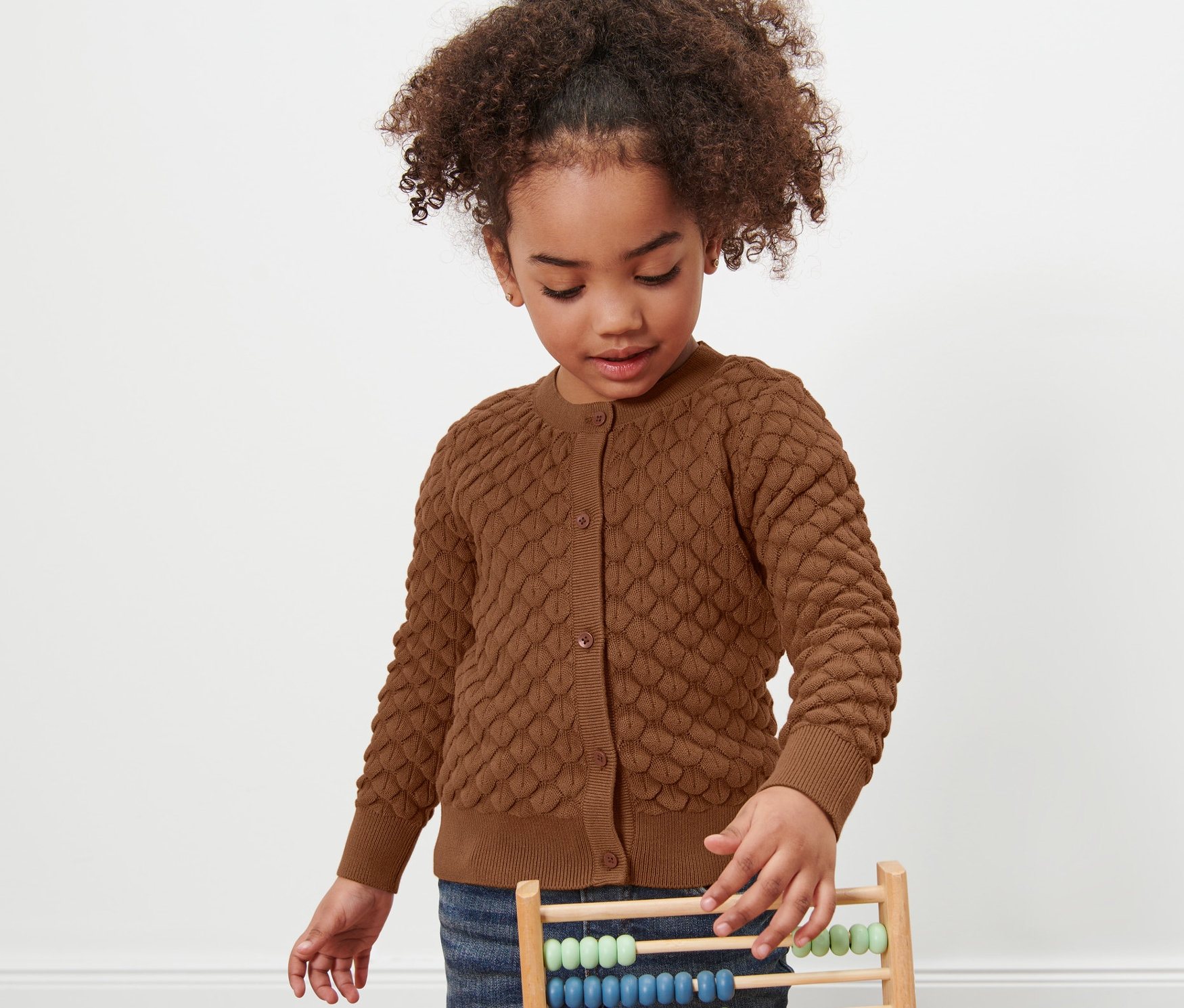 Kislány játszik egy abakusszal, barna kötött kardigánt visel.