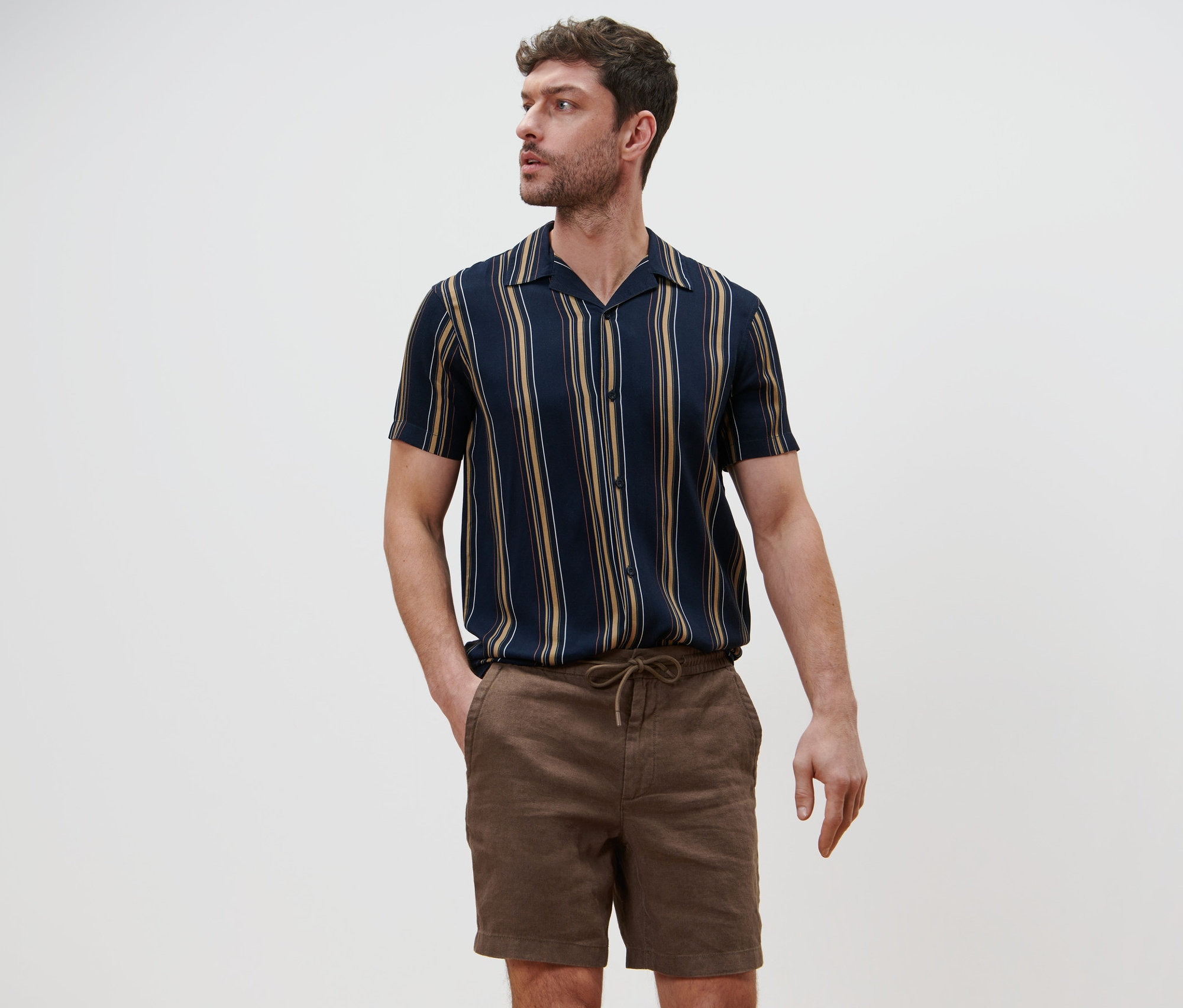Férfi pózol lenvászon rövidnadrágban és csíkos ingben.