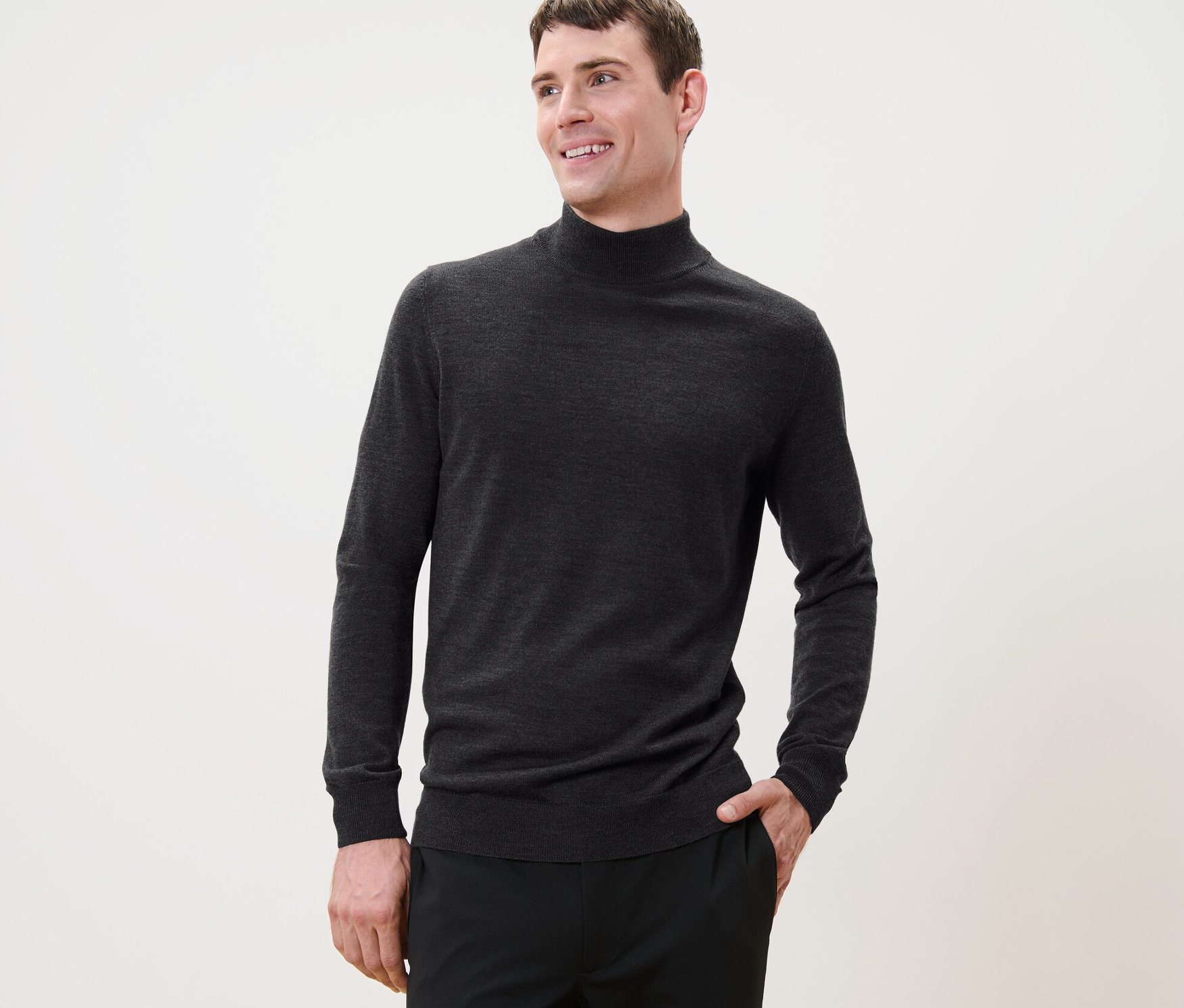 Rövid hajú férfi pózol antracit színű merinó gyapjúpulóverben és fekete nadrágban.