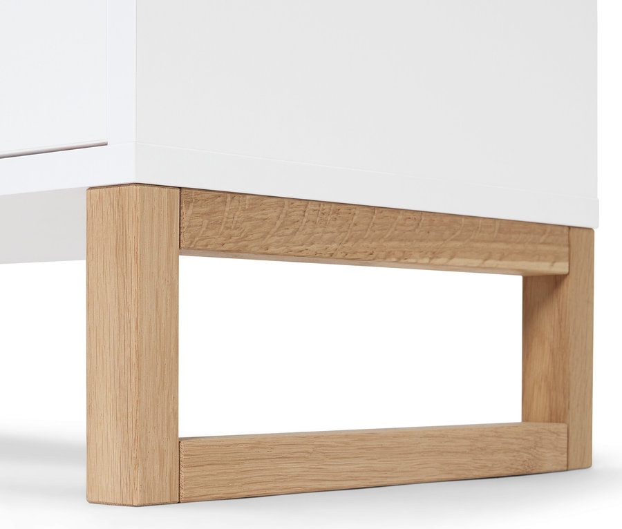 A fehér, 2 ajtós, 2 fiókos fürdőszobai komód részlete fa lábakkal.