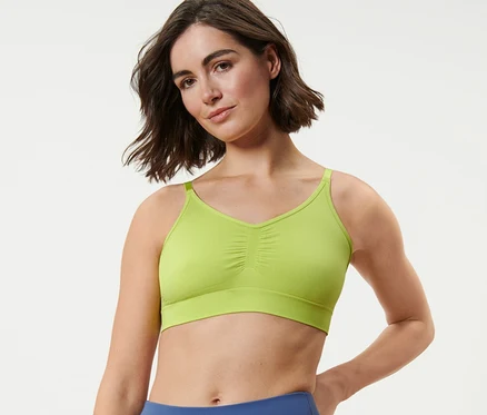 Nő visel egy Varrásmentes bustier sportmelltartót és kék leggingset.