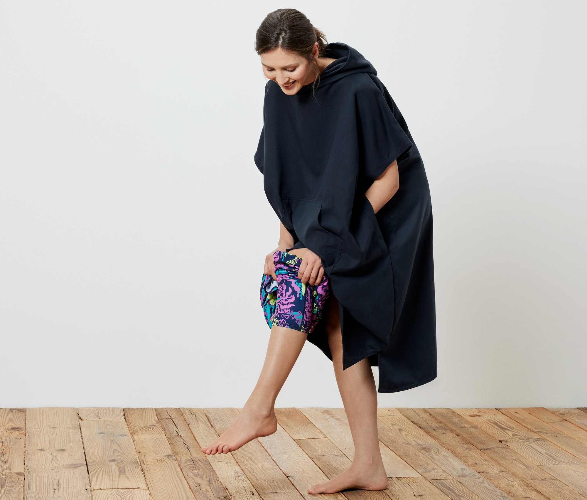 Egy mosolygó nő sötétkék mikroszálas törölköző poncsót vesz fel.