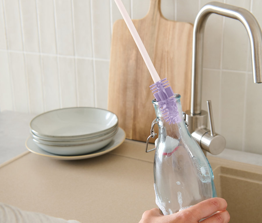 Egy kéz üveget tisztít egy üvegmosó kefével.