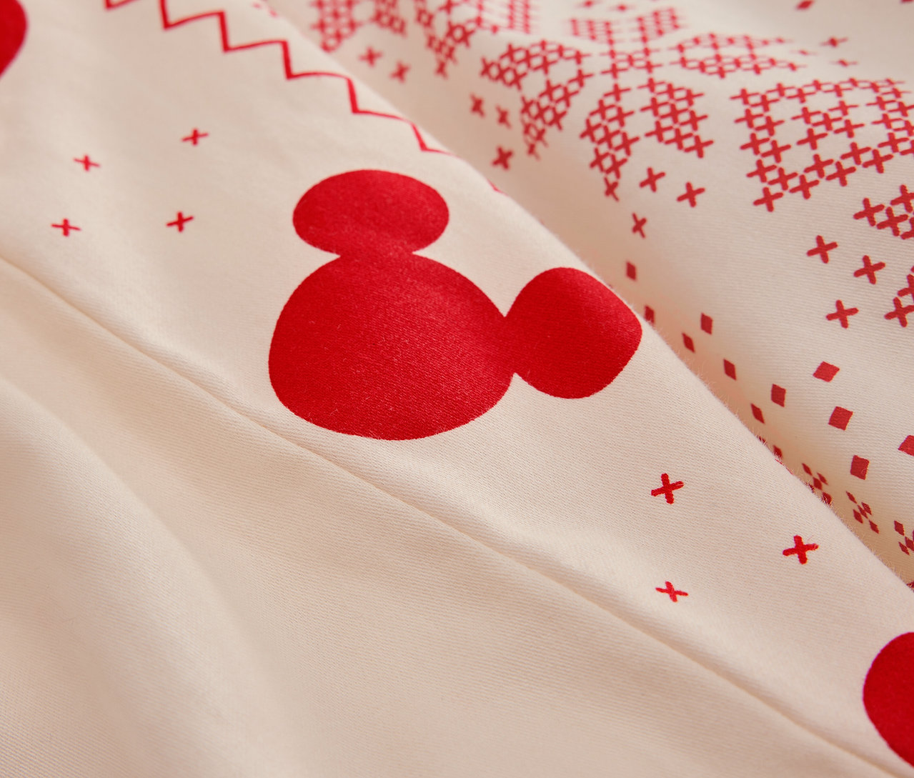 Egy fehér ágynemű részlete piros Mickey egér mintával és karácsonyi motívumokkal.