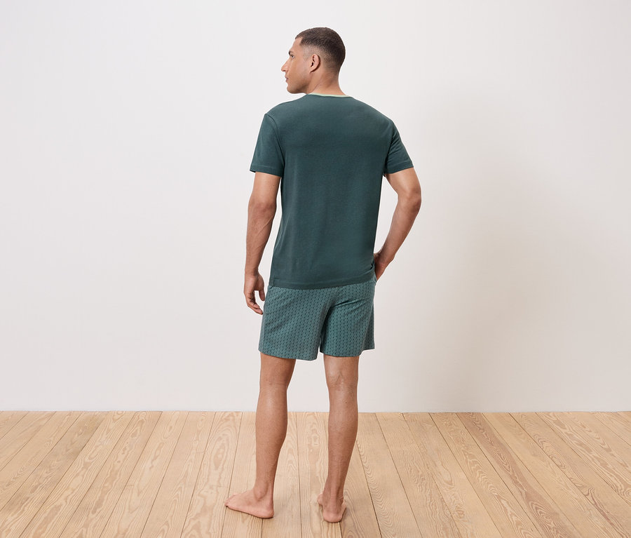 Hátulról látható férfi zöld pólót és mintás rövidnadrágot visel.