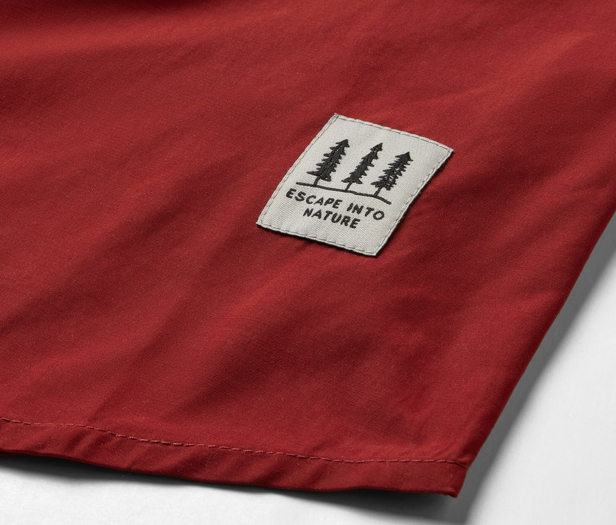 Egy piros női túrablúz részlete, fa motívummal és „ESCAPE INTO NATURE” felirattal.