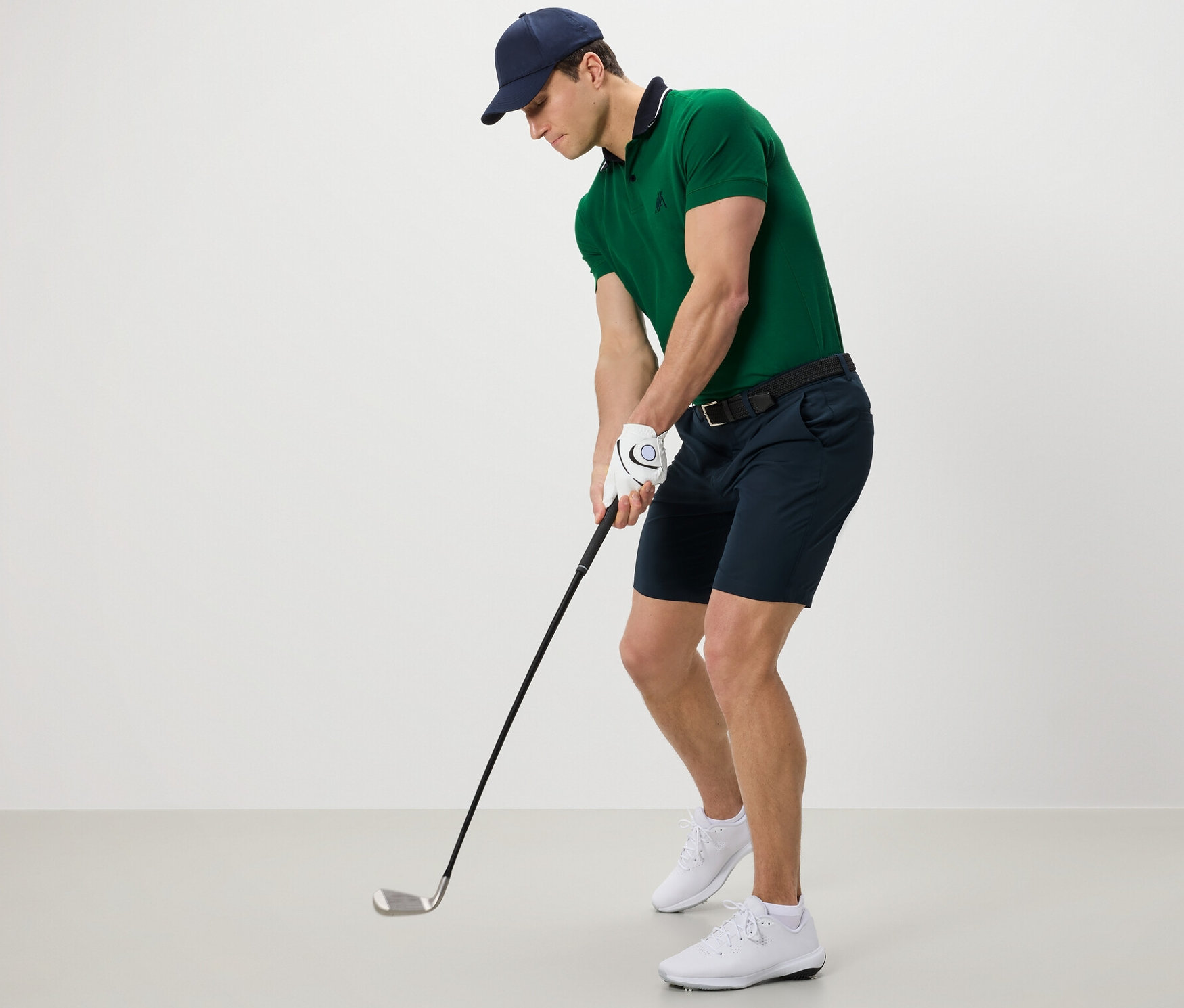 Férfi zöld pólóban és fekete funkcionális rövidnadrágban golfozik.