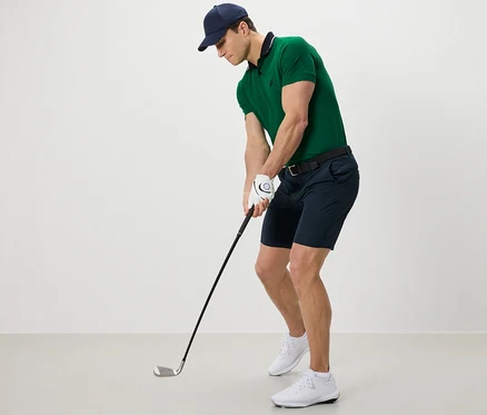 Férfi zöld pólóban és fekete funkcionális rövidnadrágban golfozik.