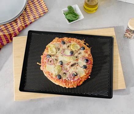 Pizza olívával, articsókával és lilahagymával egy fekete sütőlemezen egy fa vágódeszkán.
