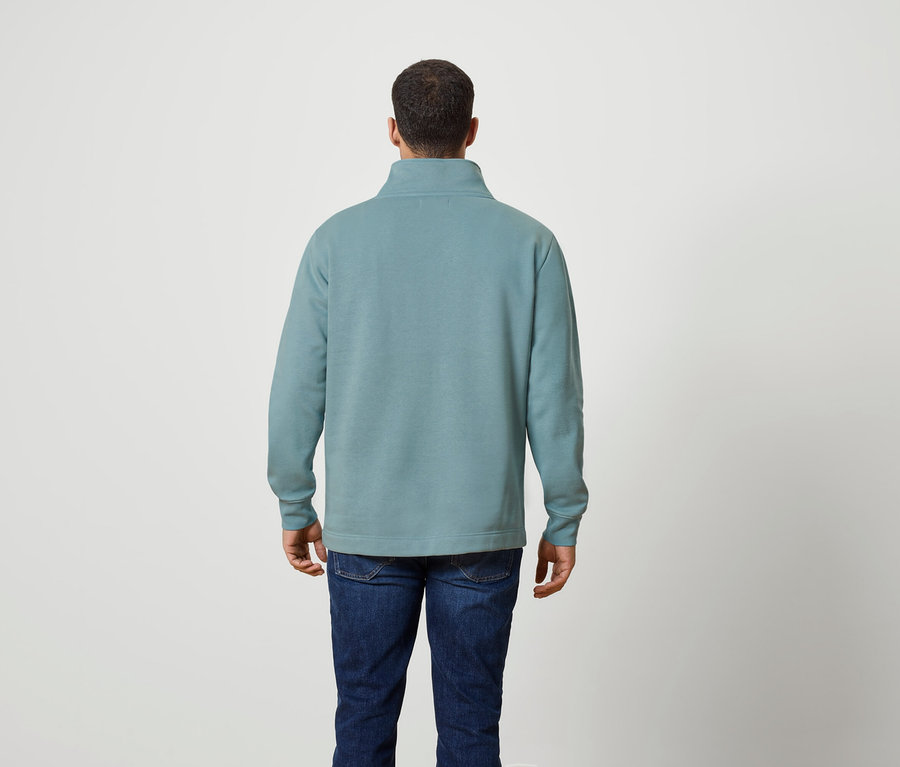 Hátulról látható férfi türkiz színű, negyed cipzáras pulóvert és farmert visel.