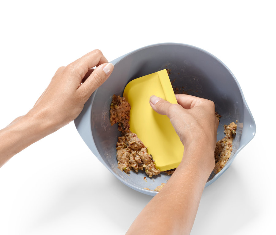 Egy pár kéz tésztát kever egy tálban egy sárga spatulával.