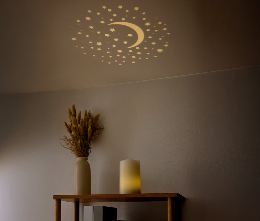 A mennyezeten csillagok és egy félhold látható. A polcon egy váza szárított virágokkal és egy gyertya található.