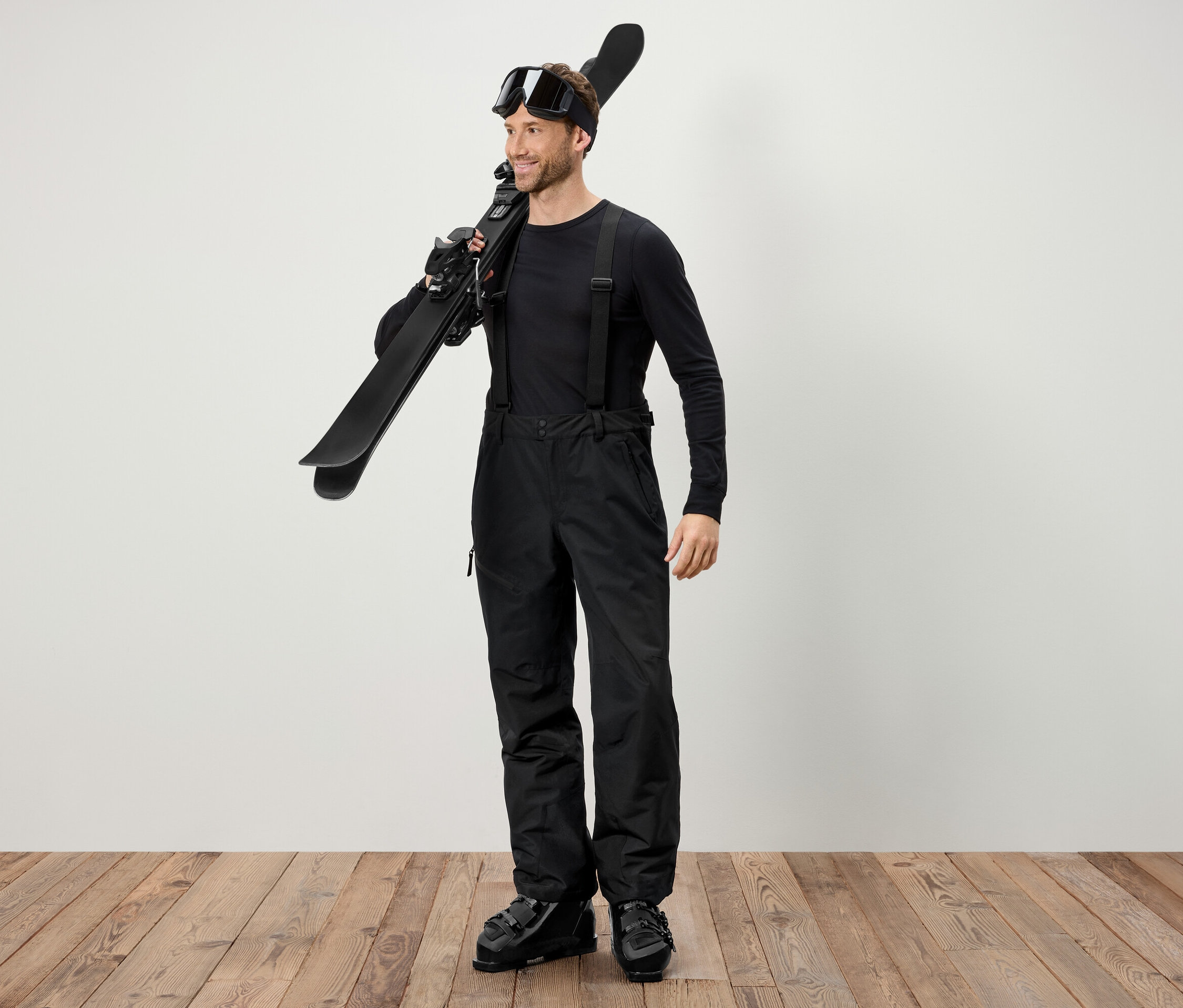 Férfi fekete síruhában síléceket visz a vállán.