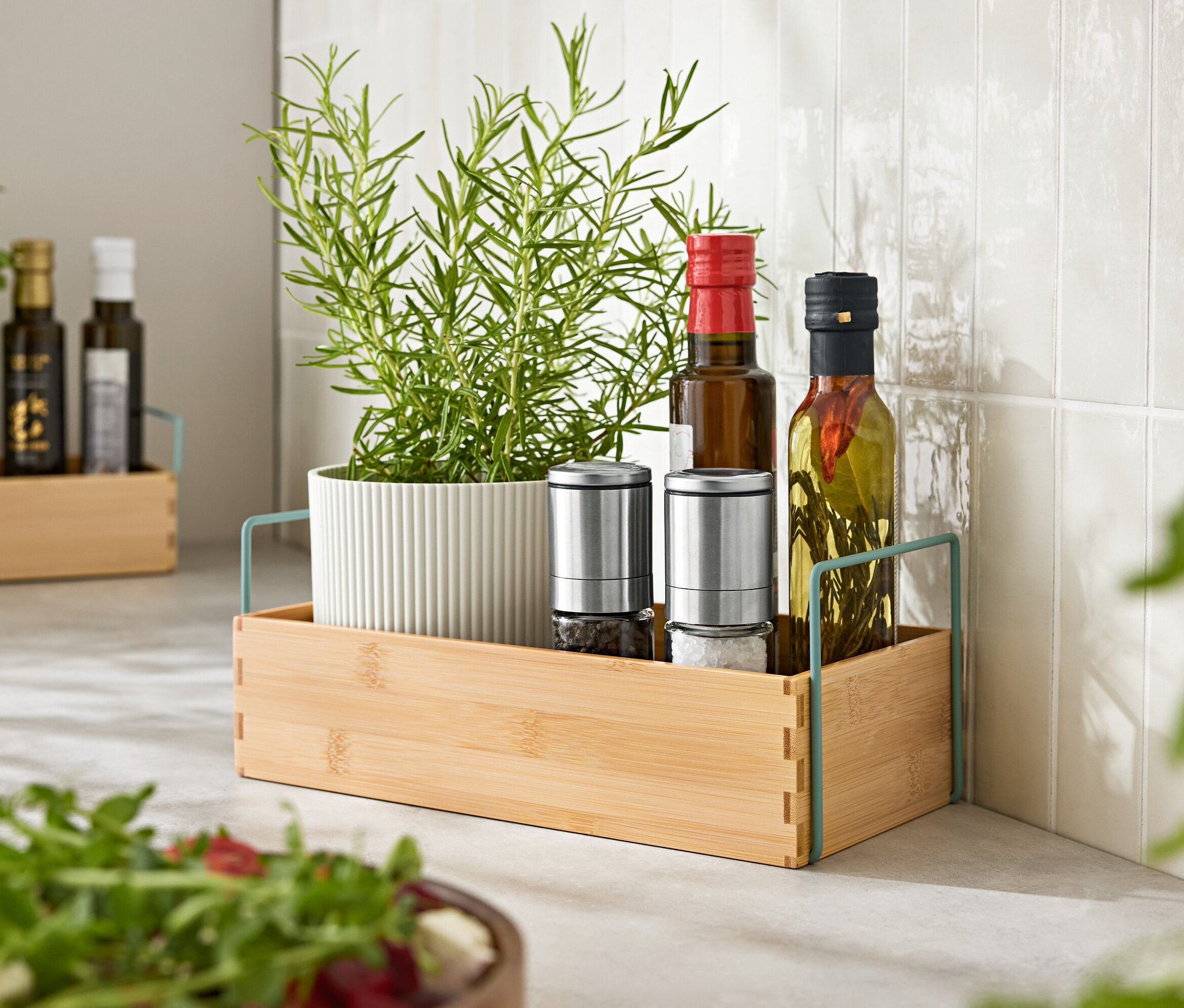 Fűszernövények cserépben, két fűszermalom és két üveg olaj egy fa tálcán.