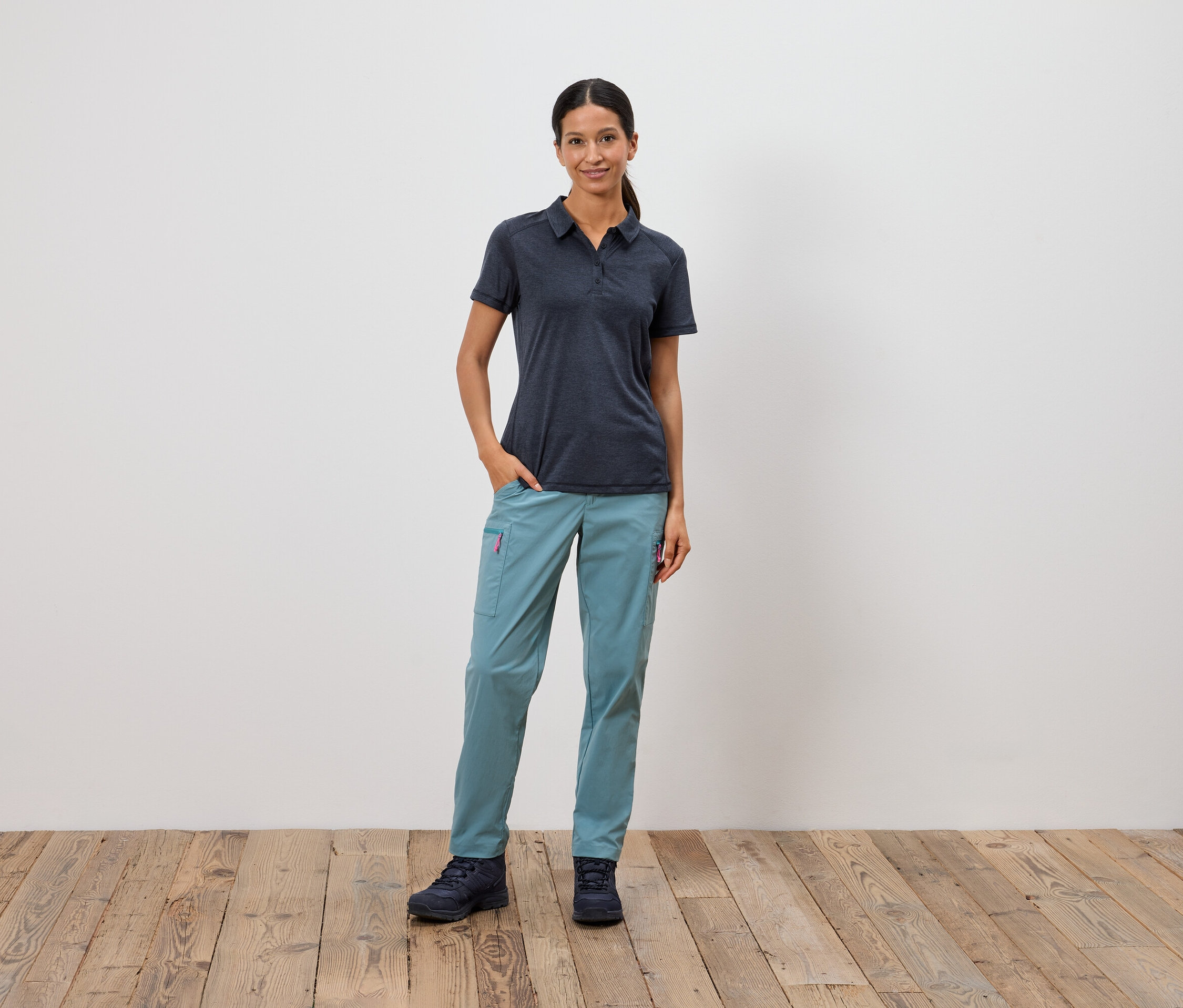 Egy nő áll kezével a zsebében egy fehér fal előtt.