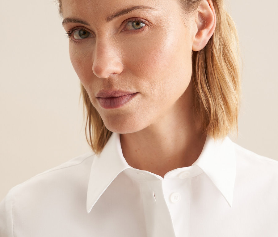 Portré egy szőke hajú nőről, aki fehér Seidensticker rövid ujjú blúzt visel.