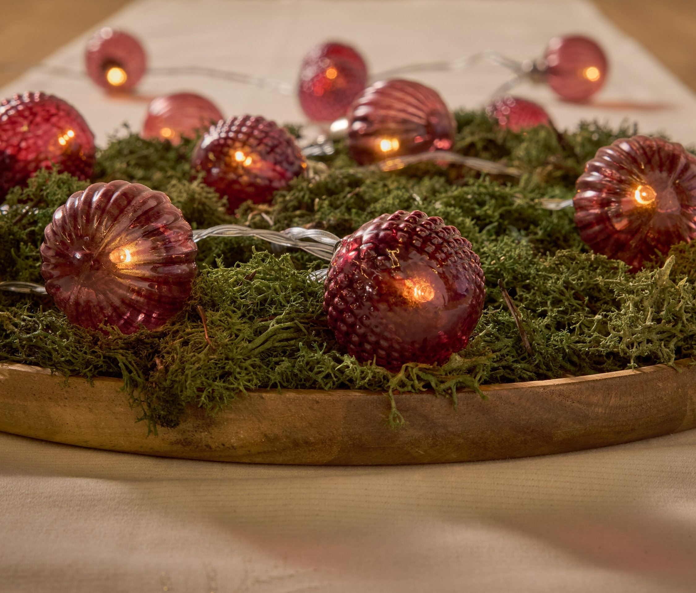 Dekoratív piros lámpák mohán, egy fából készült tálban.