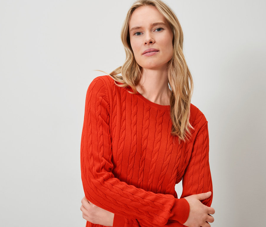 Egy szőke nő narancssárga pulóvert visel.