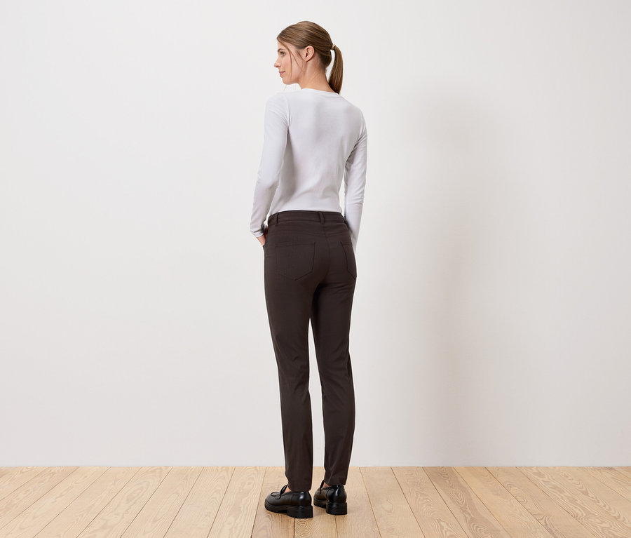 Egy nő áll háttal a kamerának, hosszú nadrágot és hosszú ujjú felsőt visel.