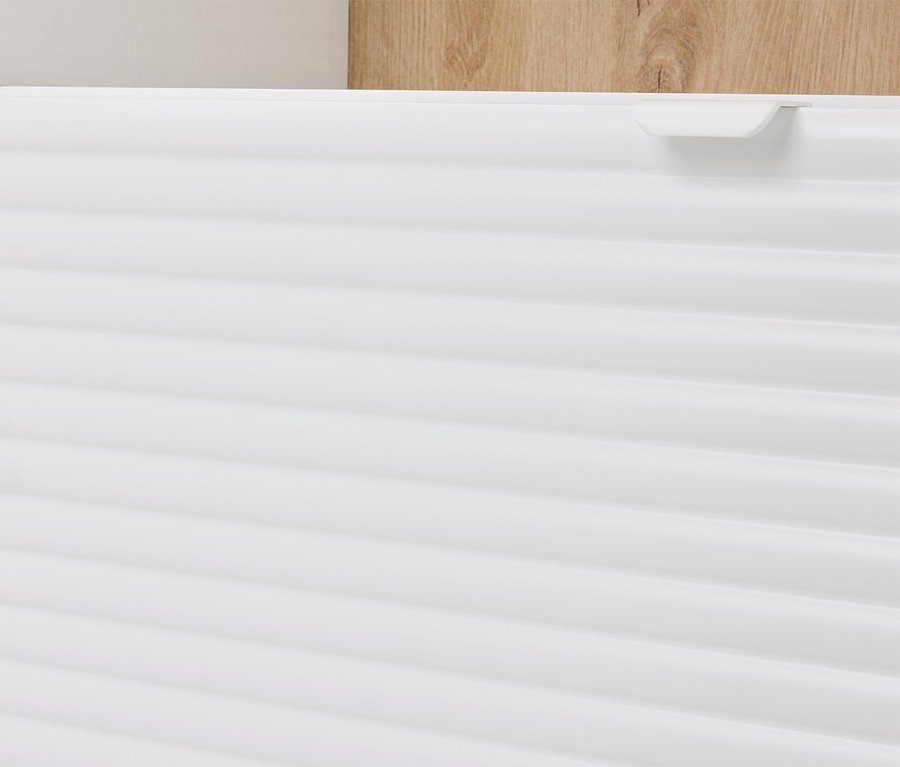 Egy vízszintes bordákkal ellátott fehér szekrény és egy világosbarna faelem közeli képe a háttérben.
