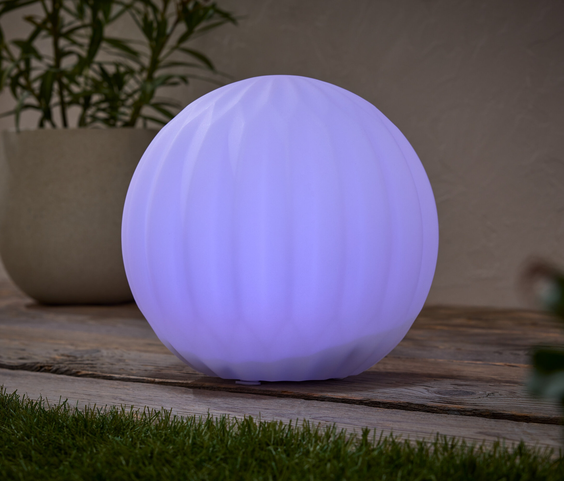 Egy kerek, lila lámpa áll egy faasztalon egy cserepes növény mellett.