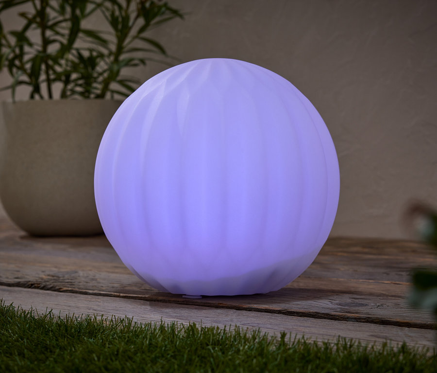 Egy kerek, lila lámpa áll egy faasztalon egy cserepes növény mellett.