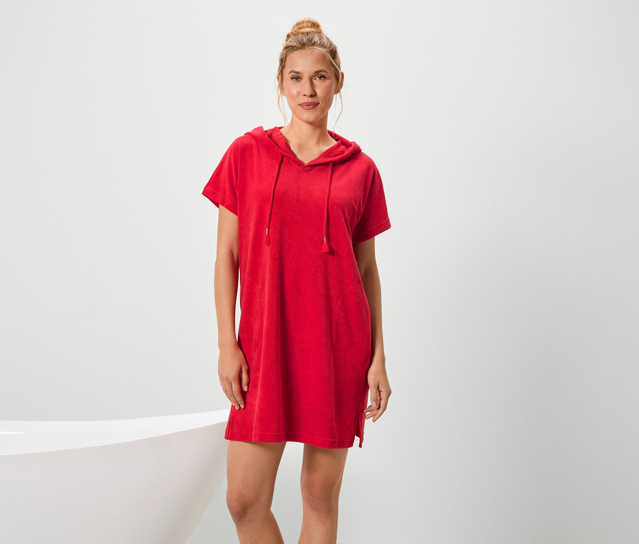 Egy nő áll egy kád mellett, és piros, rövid ujjú, kapucnis ruhát visel.