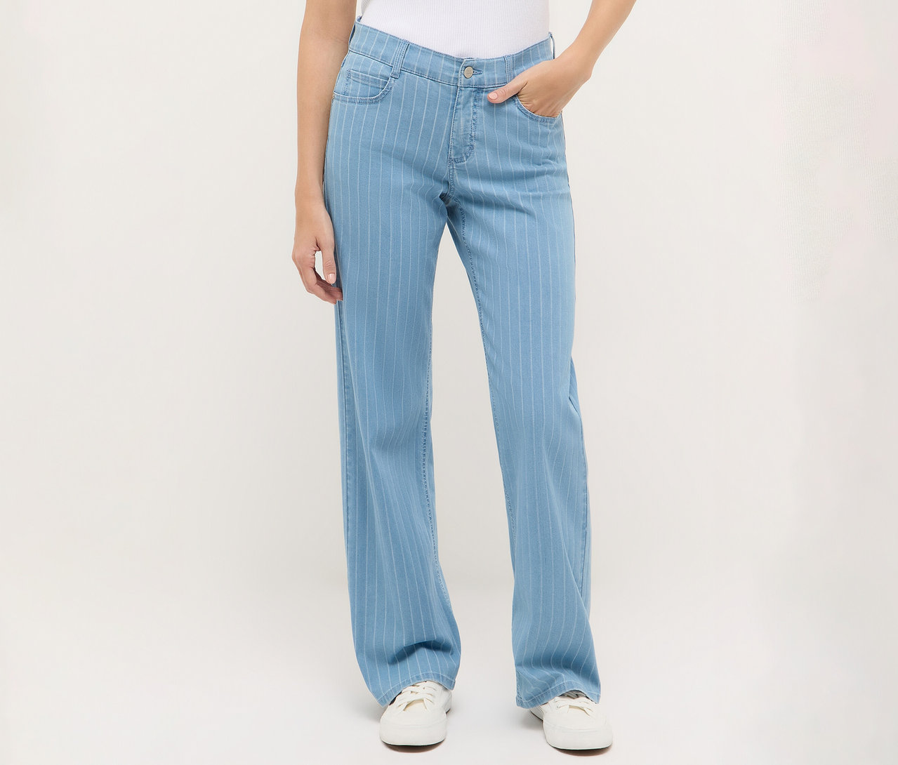 Nő visel egy csíkos, kék Angels denim »Liz« bőszárú farmert és fehér tornacipőt.